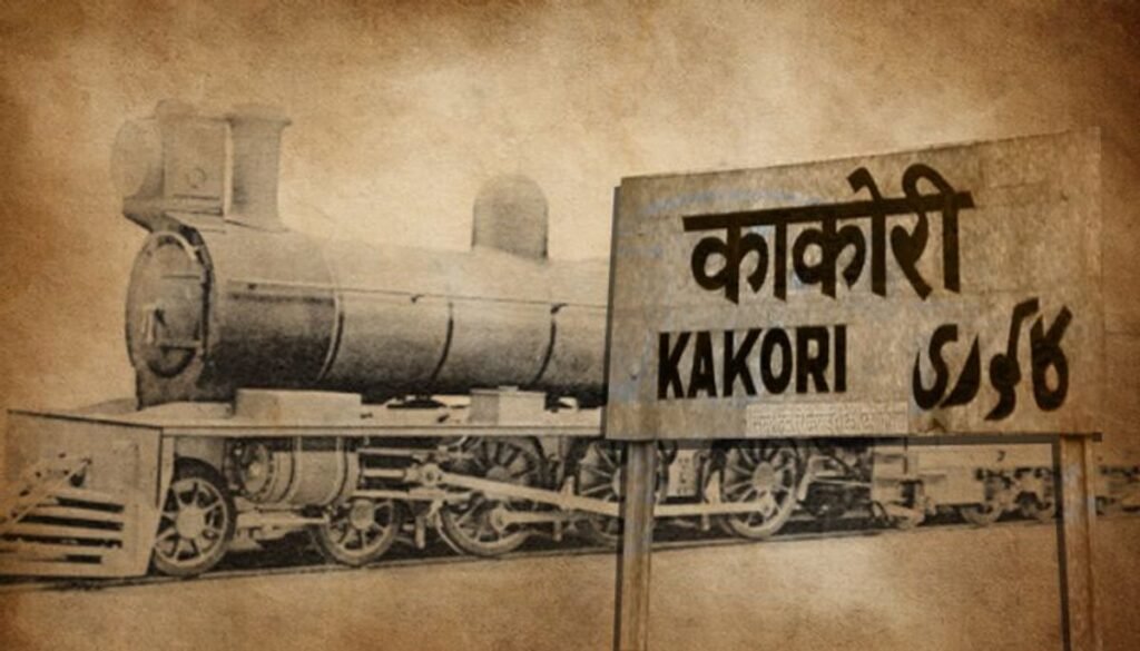 The image has a vintage, sepia tone suggesting age or historical context.
There is an illustration of an old-fashioned steam locomotive on the left side of the image.
On the right side, there is a large signboard with the word “KAKORI” written in Latin script and “काकोरी” written in Devanagari script, followed by numbers “8/9”.
The style of the locomotive and the design of the signboard give a historical feel, possibly related to the Kakori train robbery which occurred in 1925 near Kakori, now in Uttar Pradesh, India.
The background texture appears like aged paper or parchment.